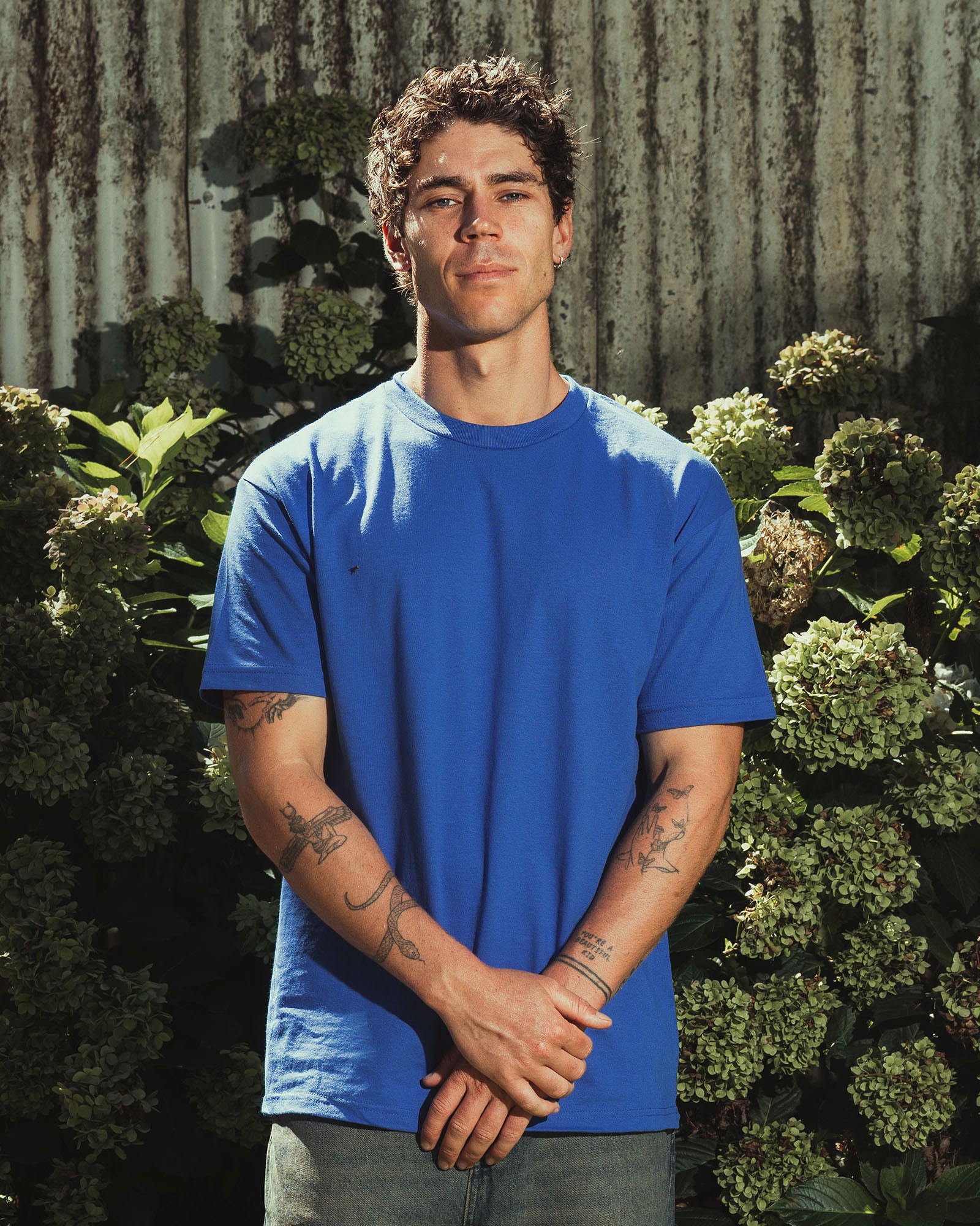 Male Model wearing a red Heavyweight Unisex Short Sleeve Crew Neck Tee, paired with blue jeans, standing against a plain background (front pose) -royal