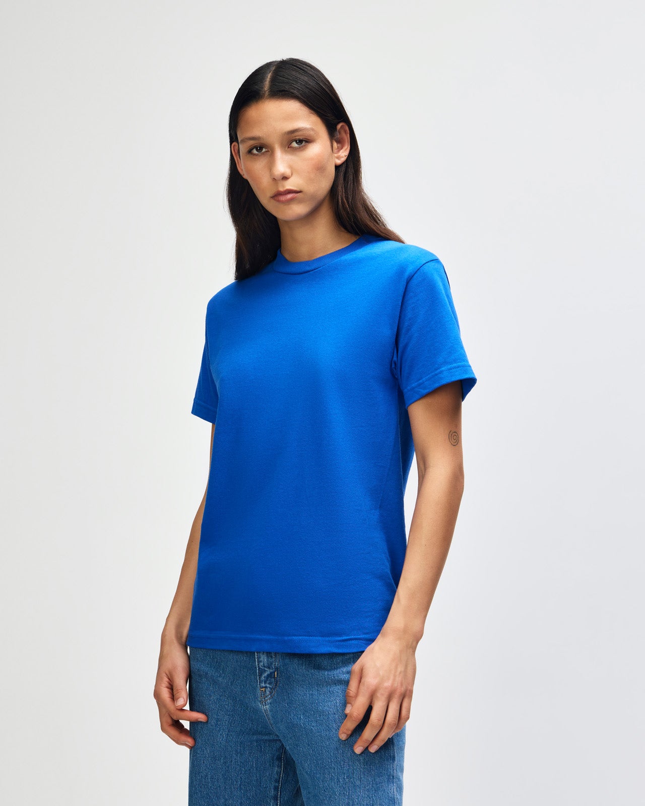Female Model wearing a red Heavyweight Unisex Short Sleeve Crew Neck Tee, paired with blue jeans, standing against a plain background (front pose) -royal