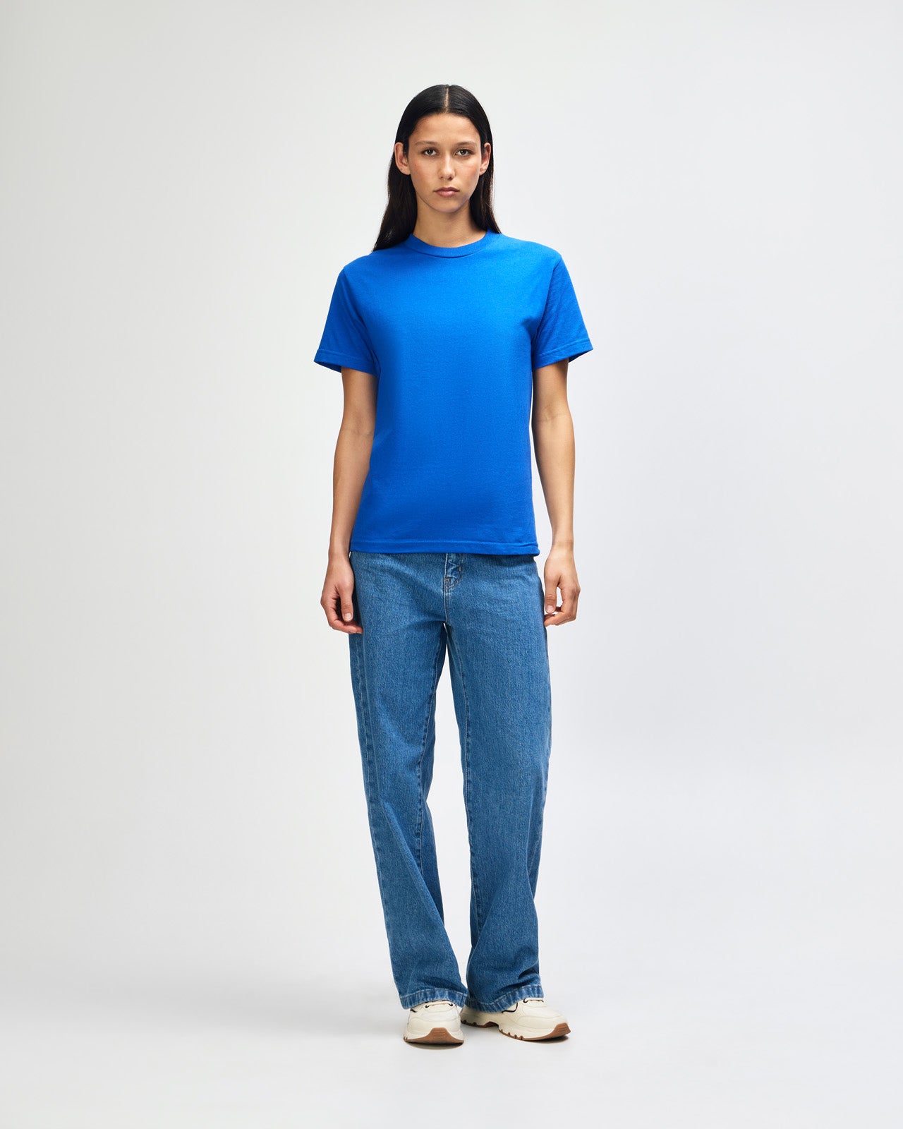 Female Model wearing a red Heavyweight Unisex Short Sleeve Crew Neck Tee, paired with blue jeans, standing against a plain background (front pose) -royal