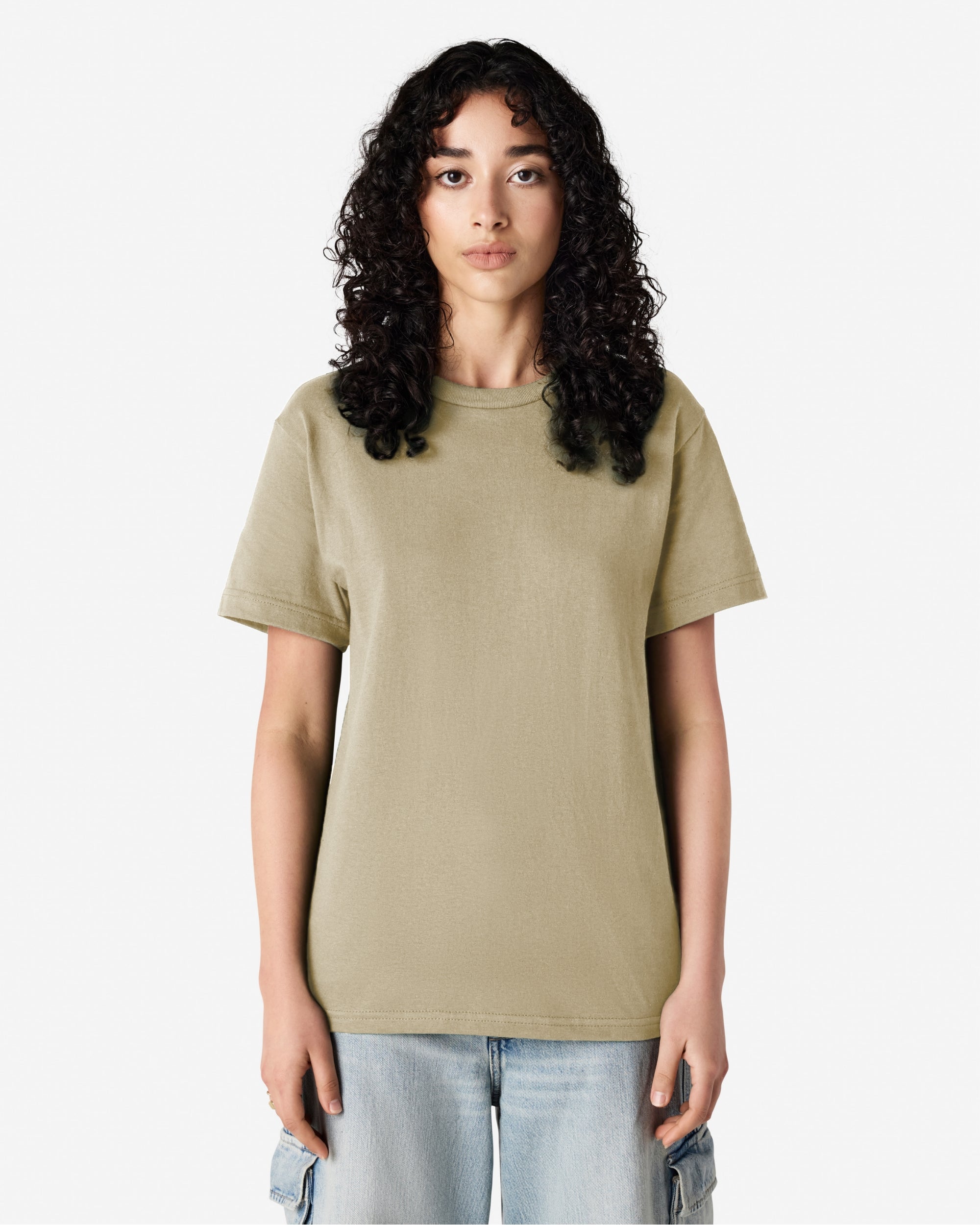 Female Model wearing a Sand Heavyweight Unisex Short Sleeve Crew Neck Tee, paired with blue jeans, standing against a plain background (front pose) -sand