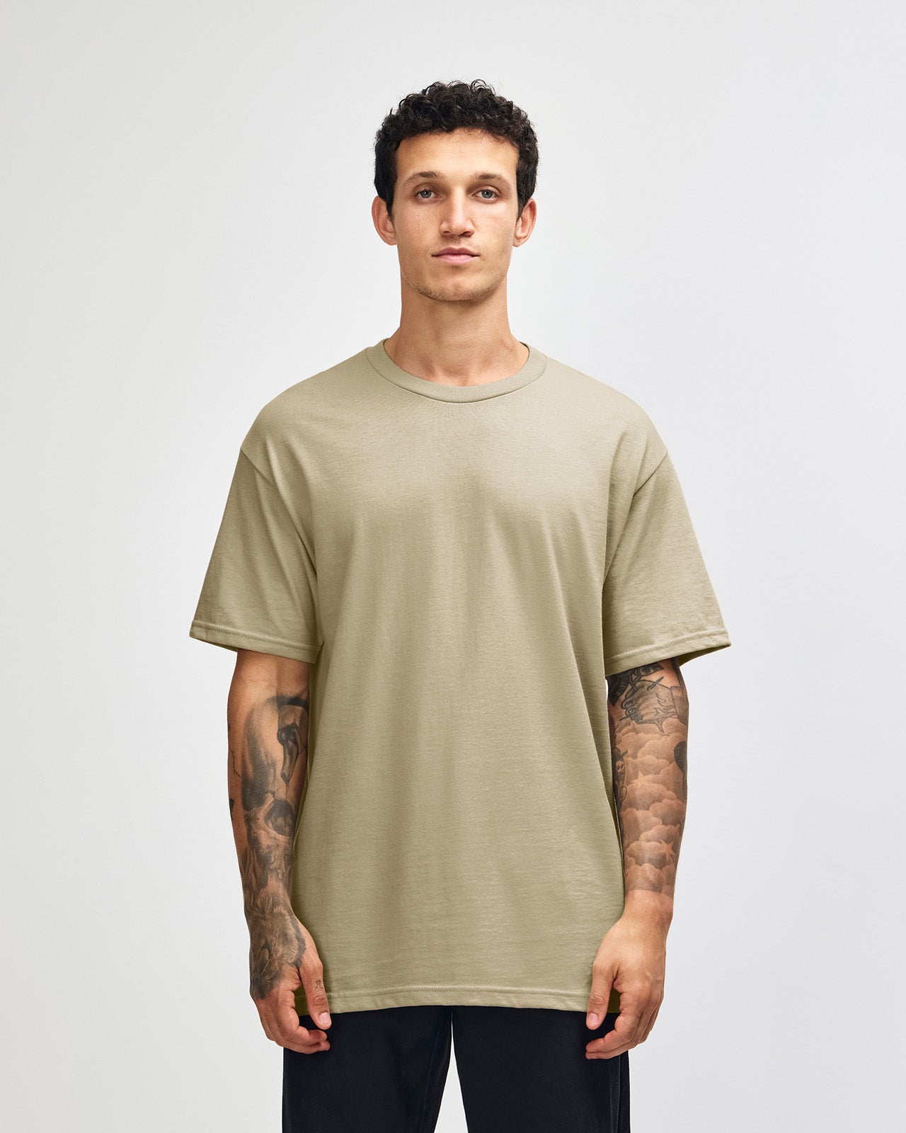 Male Model wearing a Sand Heavyweight Unisex Short Sleeve Crew Neck Tee, paired with blue jeans, standing against a plain background (front pose) -sand