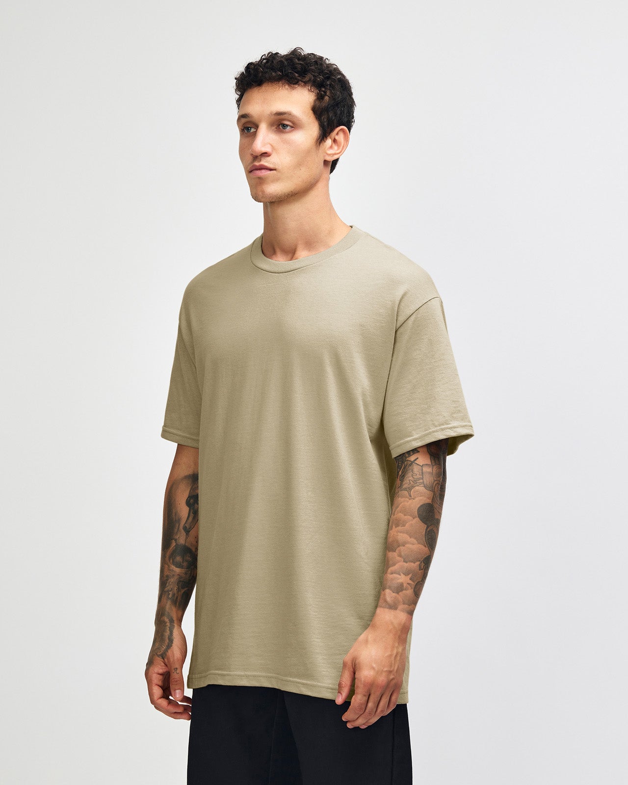 Male Model wearing a Sand Heavyweight Unisex Short Sleeve Crew Neck Tee, paired with blue jeans, standing against a plain background (front pose) -sand