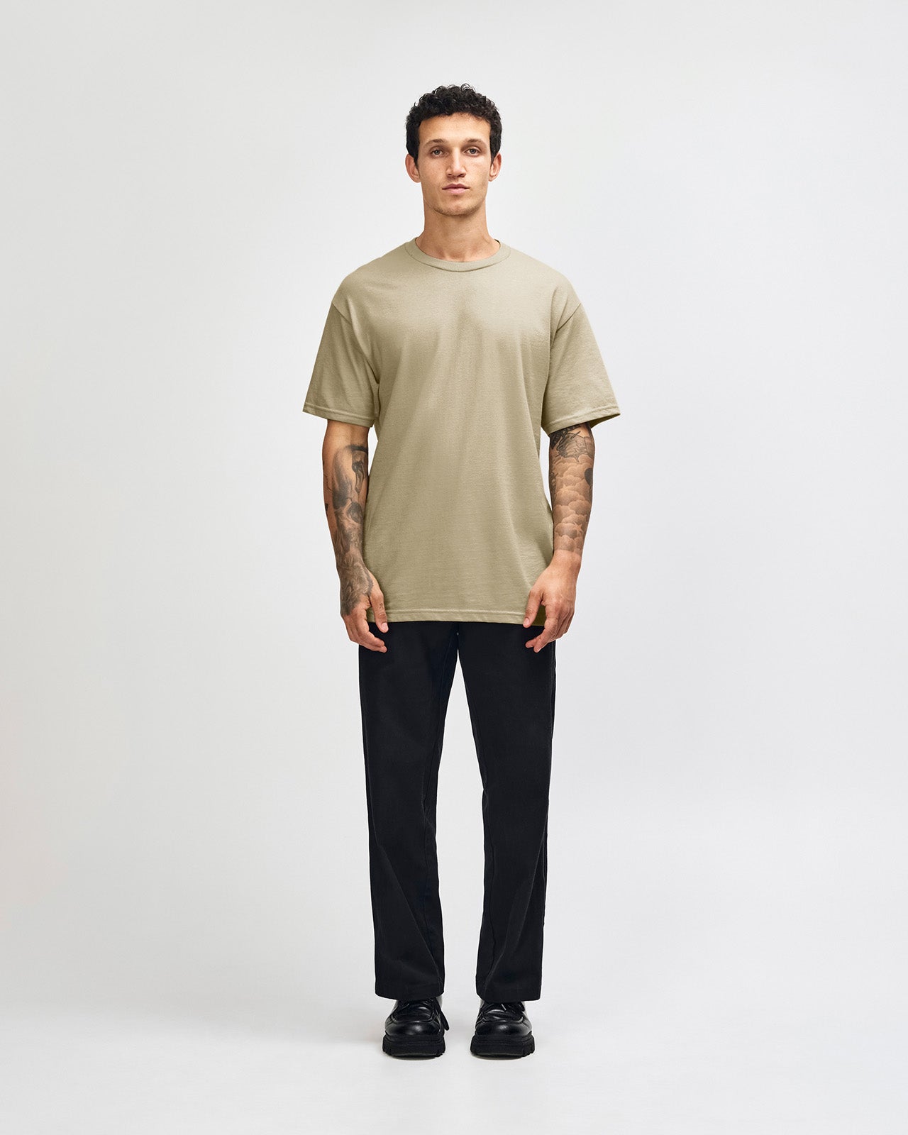 Male Model wearing a Sand Heavyweight Unisex Short Sleeve Crew Neck Tee, paired with blue jeans, standing against a plain background (front pose) -sand