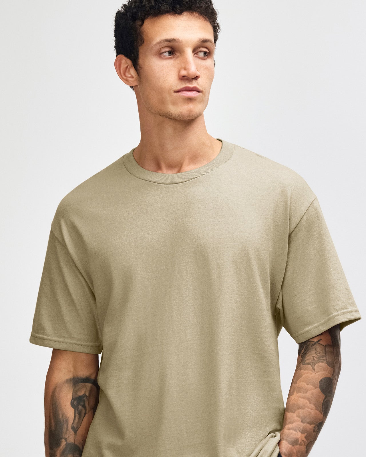 Male Model wearing a Sand Heavyweight Unisex Short Sleeve Crew Neck Tee, paired with blue jeans, standing against a plain background (front pose) -sand