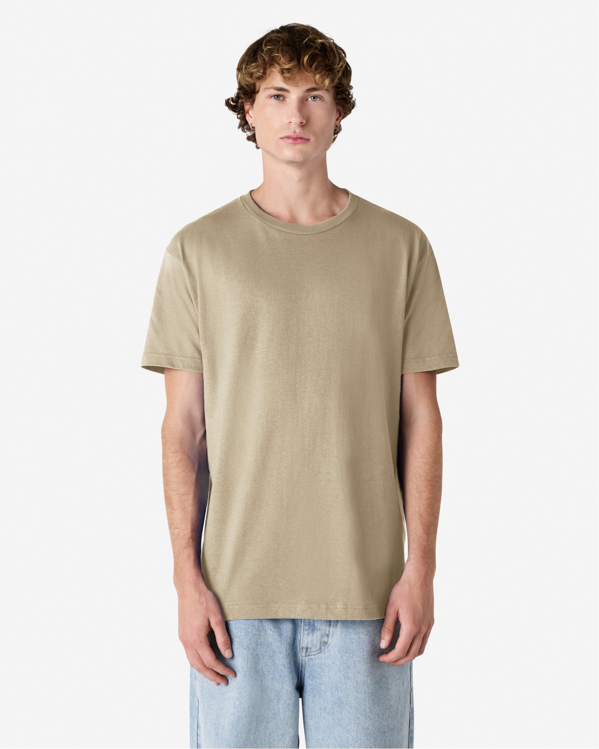 Male Model wearing a Sand Heavyweight Unisex Short Sleeve Crew Neck Tee, paired with blue jeans, standing against a plain background (front pose) -sand