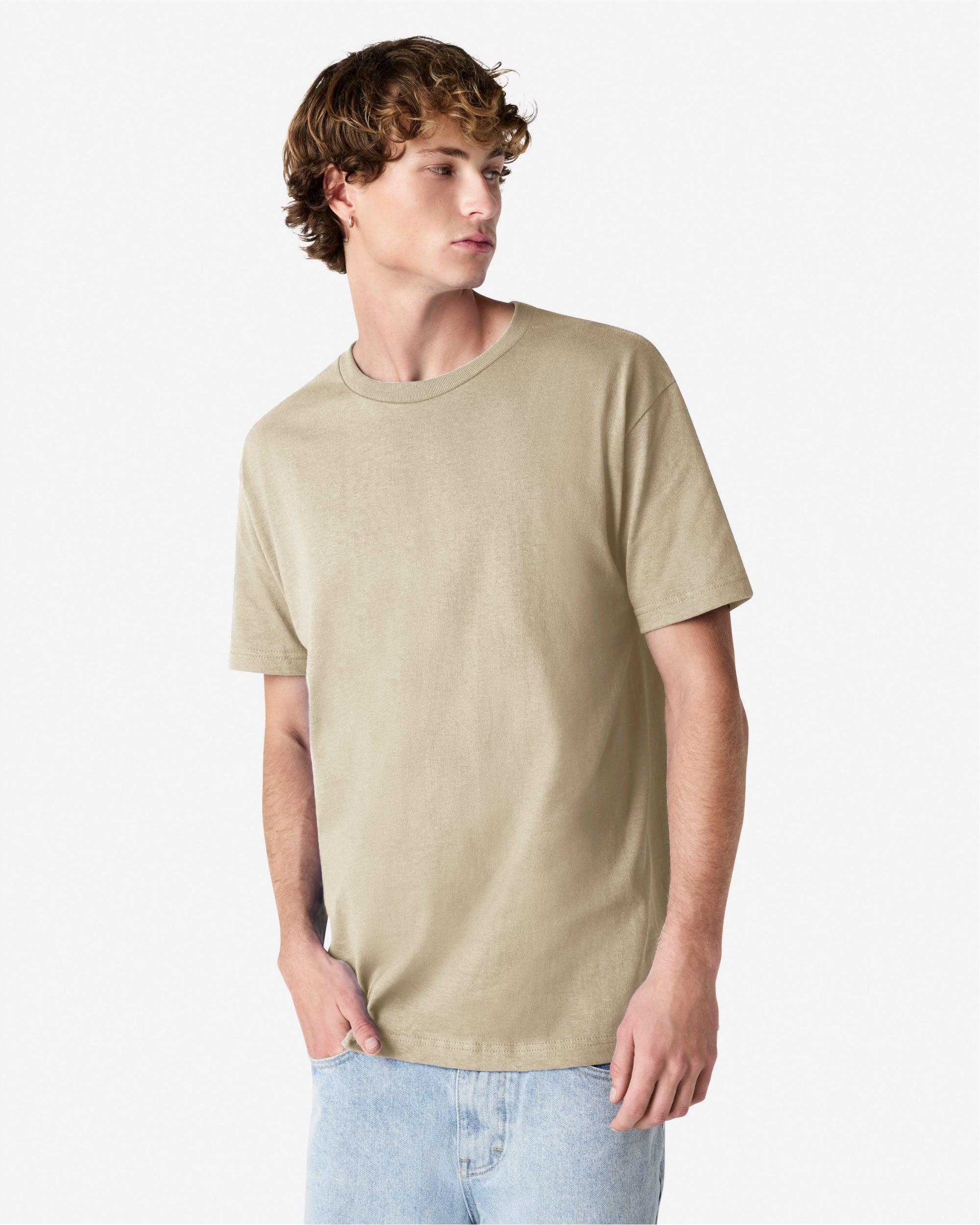 Male Model wearing a Sand Heavyweight Unisex Short Sleeve Crew Neck Tee, paired with blue jeans, standing against a plain background (front pose) -sand