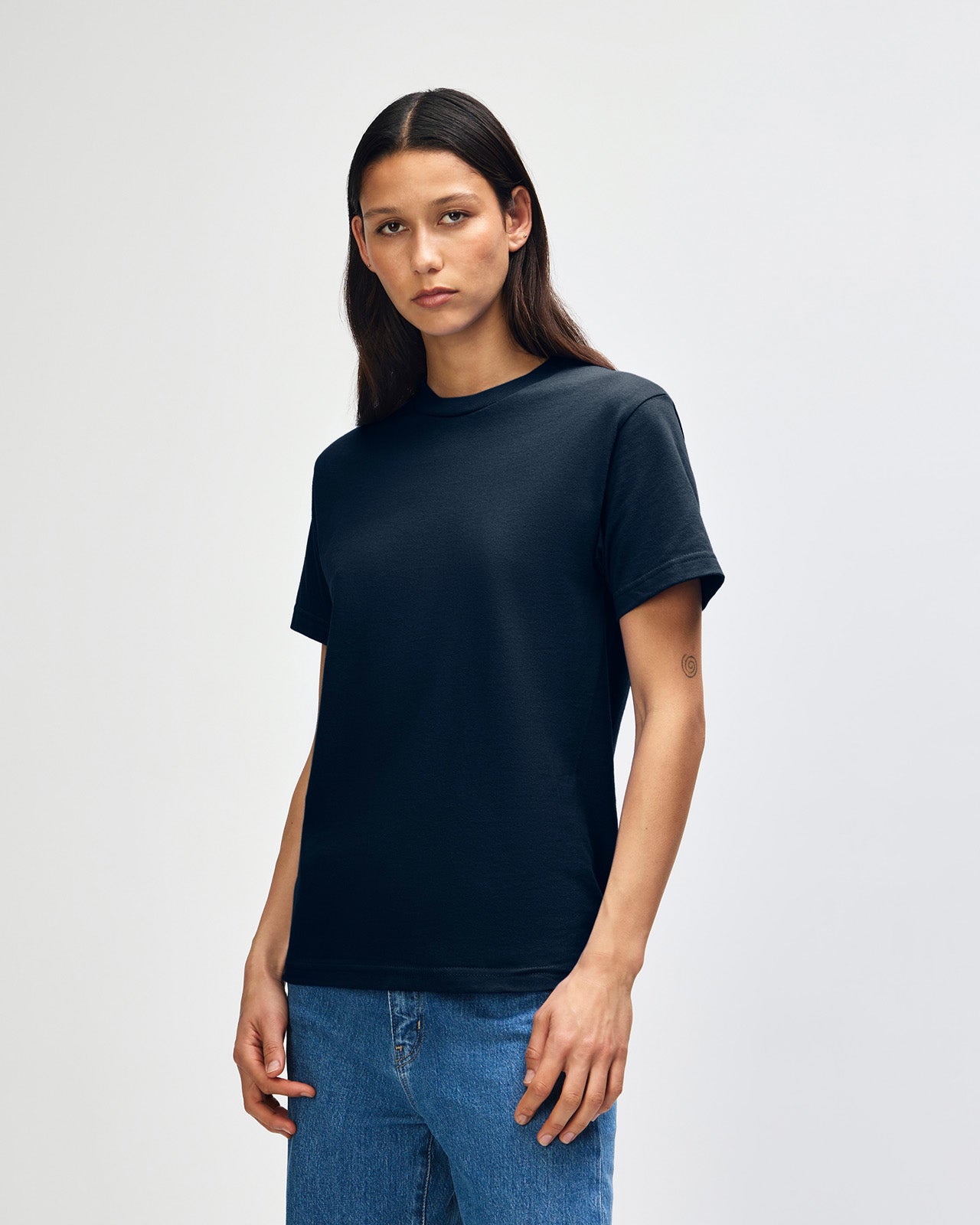 Female Model wearing a True Navy Heavyweight Unisex Short Sleeve Crew Neck Tee, paired with blue jeans, standing against a plain background (front pose) -true navy