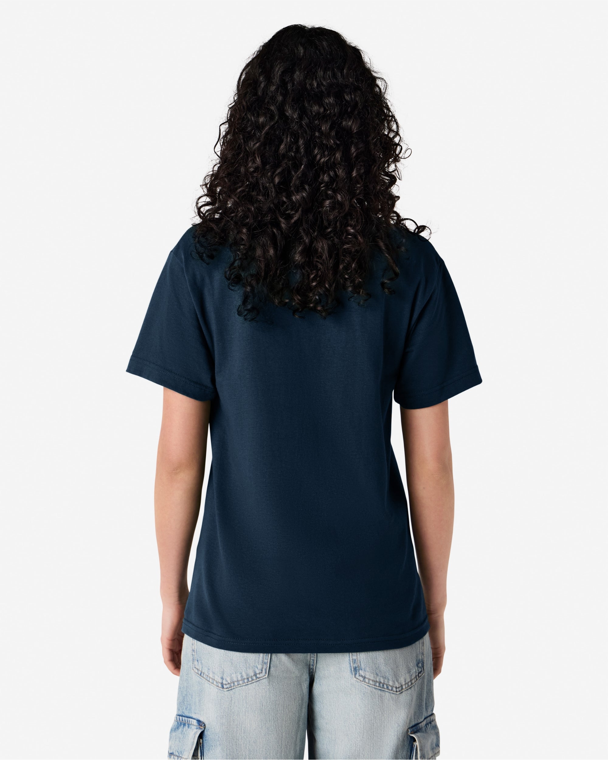 Female Model wearing a True Navy Heavyweight Unisex Short Sleeve Crew Neck Tee, paired with blue jeans, standing against a plain background (back pose) -true navy