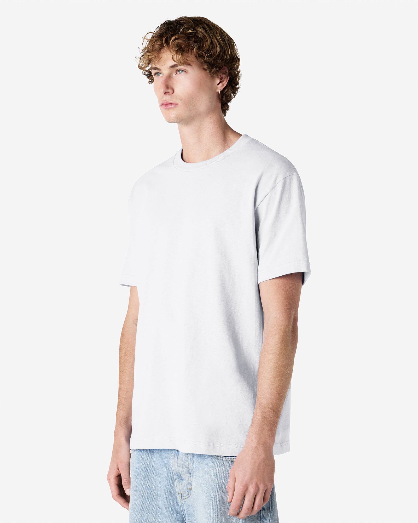 Male Model wearing a White Heavyweight Unisex Short Sleeve Crew Neck Tee, paired with blue jeans, standing against a plain background (front pose) -white