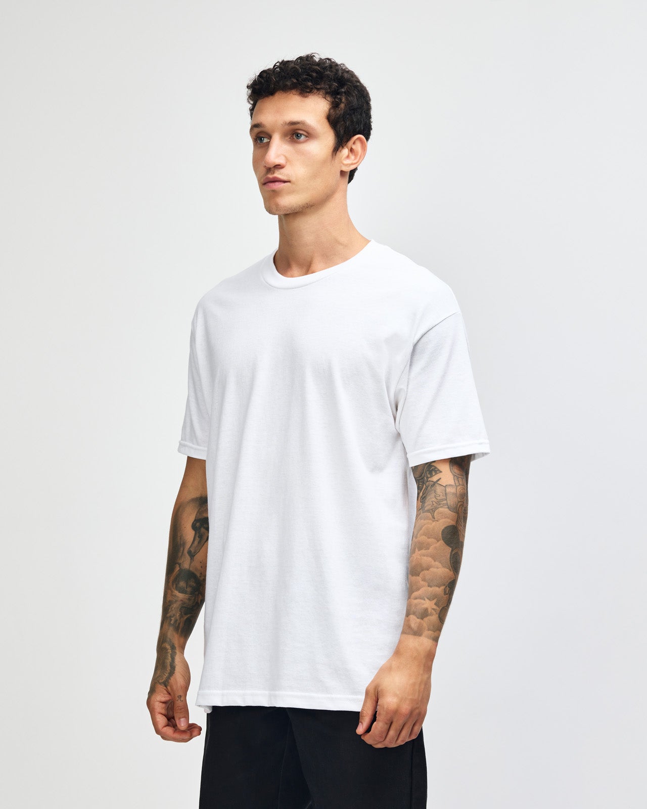 Male Model wearing a white Heavyweight Unisex Short Sleeve Crew Neck Tee, paired with blue jeans, standing against a plain background (front pose) -white