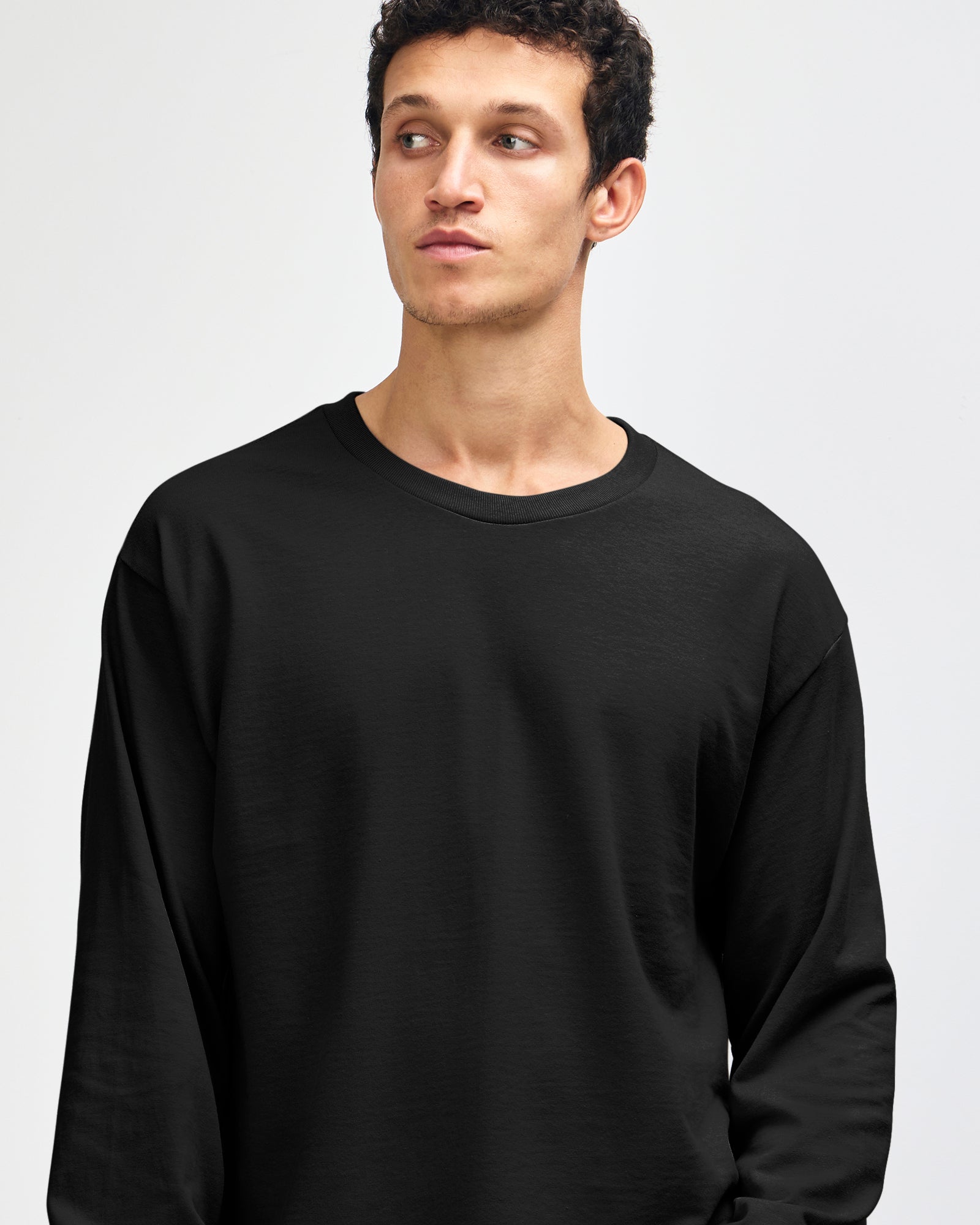 front view of a male Model wearing a black coloured Heavyweight Unisex Long Sleeve Crew Neck Tee, paired with blue jeans, standing against a plain background (front pose) -black