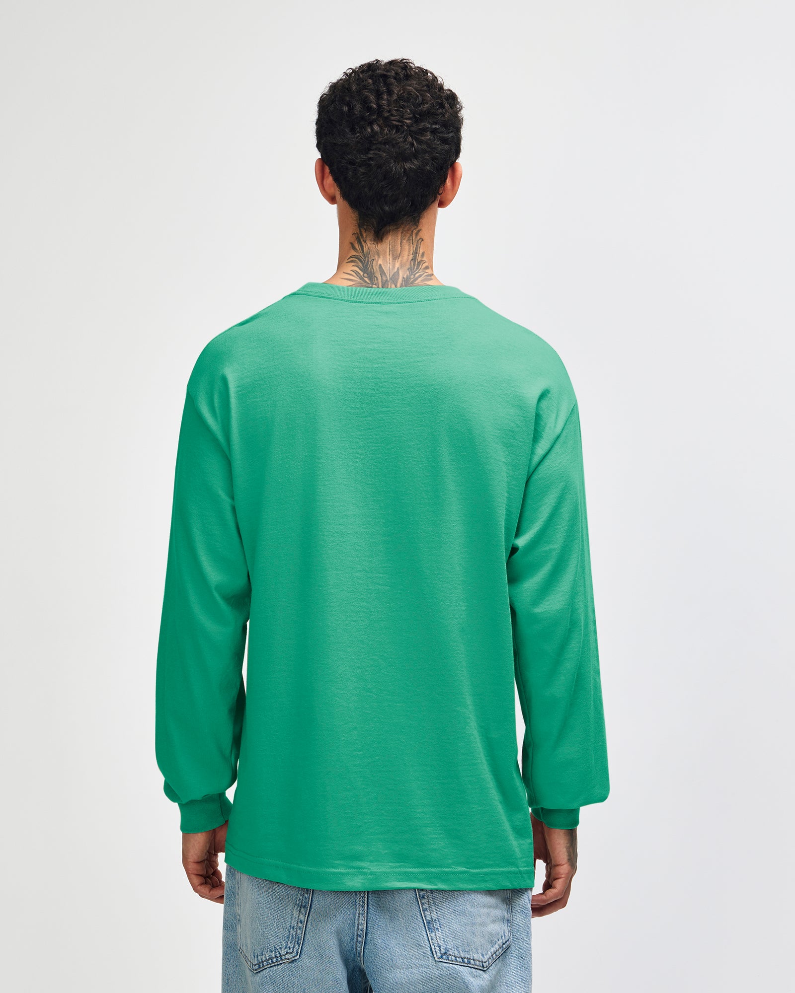 back view of a male Model wearing a Celadon colored Heavyweight Unisex Long Sleeve Crew Neck Tee, paired with blue jeans, standing against a plain background (back pose) -celadon