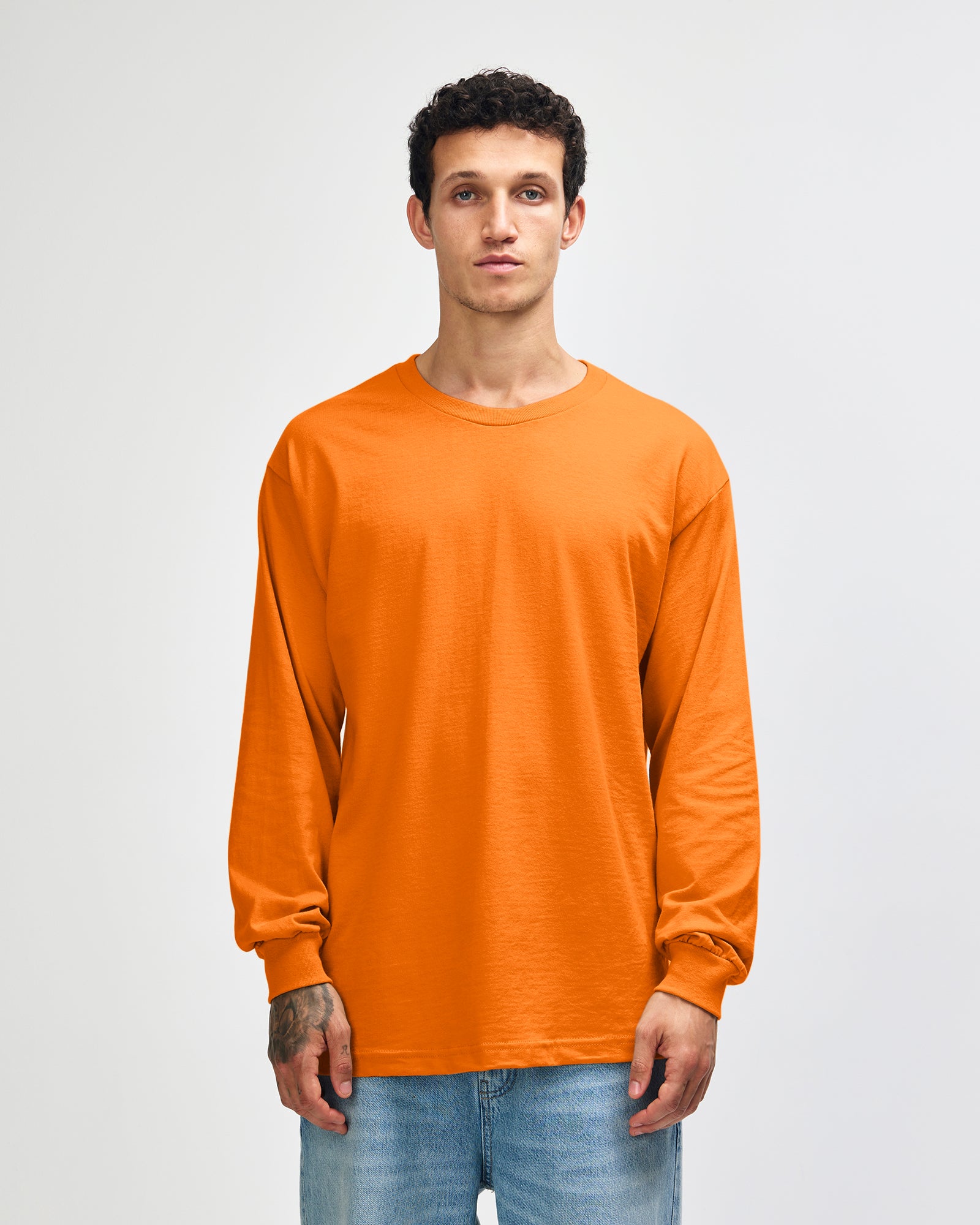 front view of a male Model wearing a Heather Orange Heavyweight Unisex Long Sleeve Crew Neck Tee, paired with blue jeans, standing against a plain background (front pose) -orange