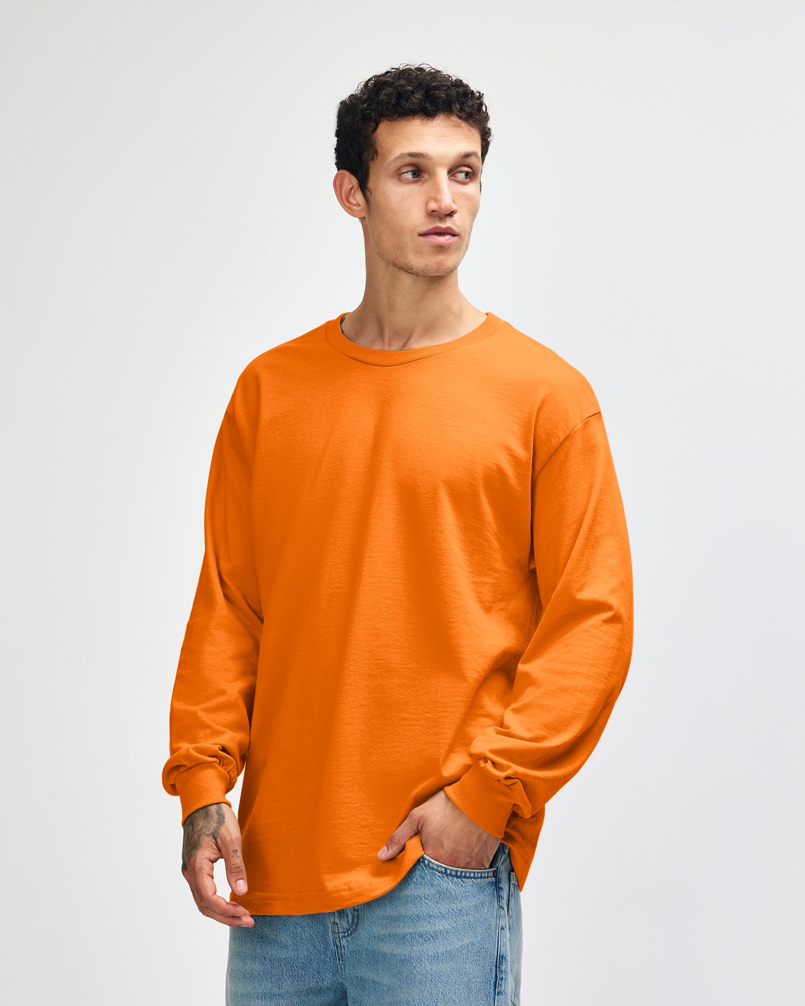 front view of a male Model wearing a Heather Orange Heavyweight Unisex Long Sleeve Crew Neck Tee, paired with blue jeans, standing against a plain background (front pose) -orange