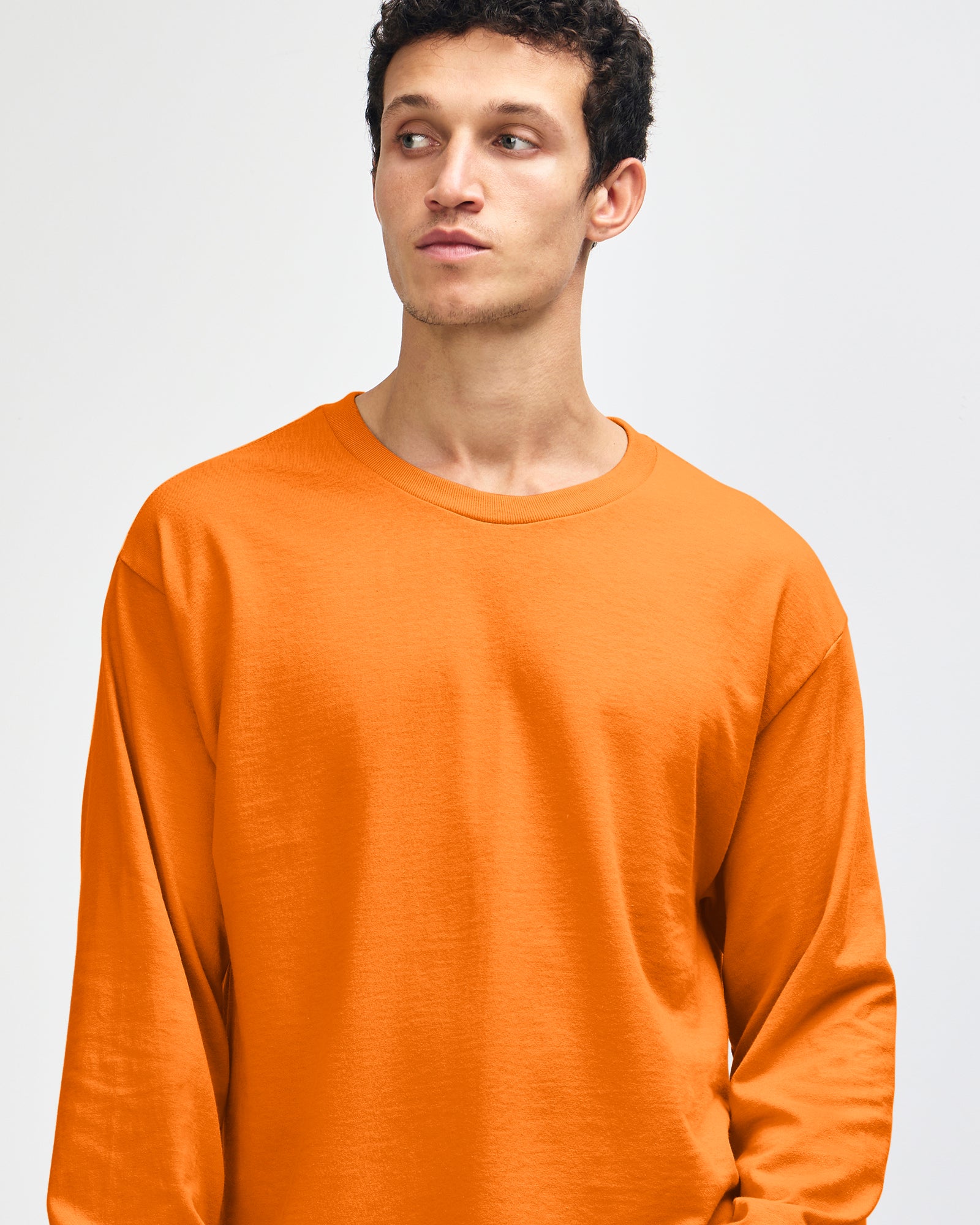 front view of a male Model wearing a Heather Orange Heavyweight Unisex Long Sleeve Crew Neck Tee, paired with blue jeans, standing against a plain background (front pose) -orange