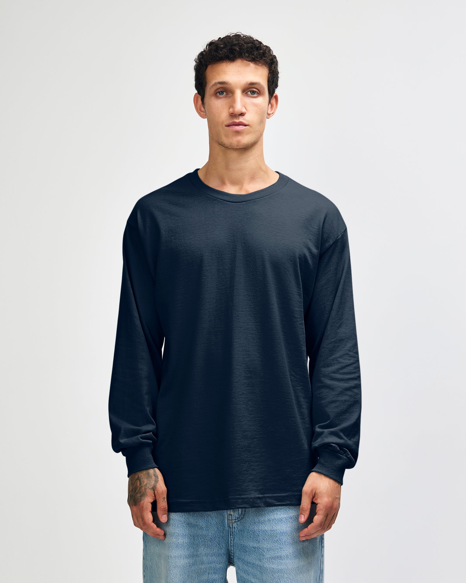 front view of a male Model wearing a True Navy colored Heavyweight Unisex Long Sleeve Crew Neck Tee, paired with blue jeans, standing against a plain background (front pose) -true navy