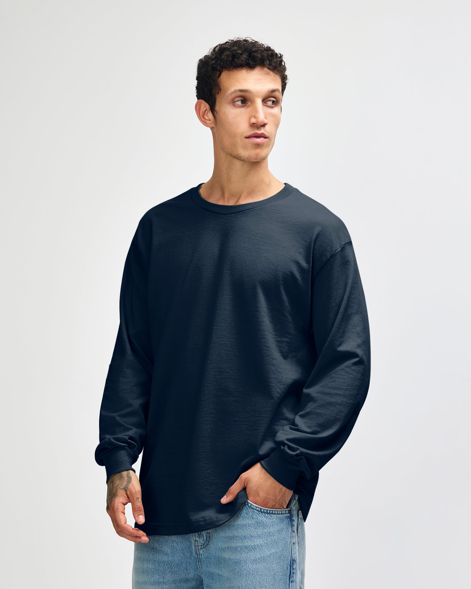 front view of a male Model wearing a True Navy colored Heavyweight Unisex Long Sleeve Crew Neck Tee, paired with blue jeans, standing against a plain background (front pose) -true navy