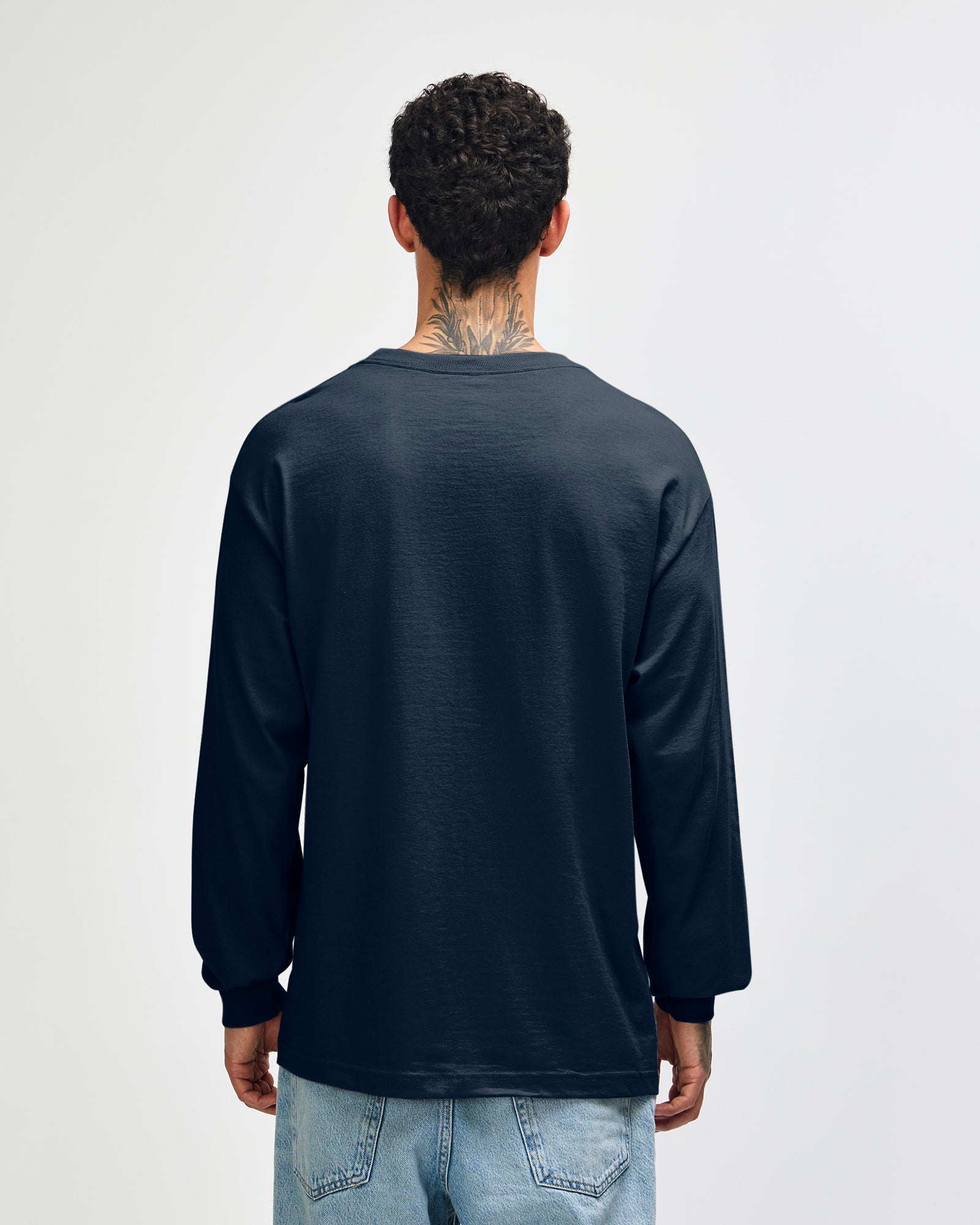 back view of a male Model wearing a True Navy colored Heavyweight Unisex Long Sleeve Crew Neck Tee, paired with blue jeans, standing against a plain background (back pose) -true navy