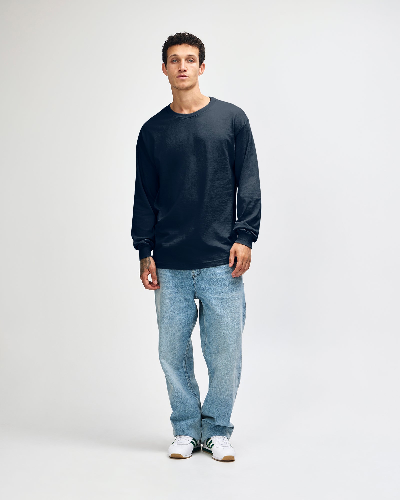 front view of a male Model wearing a True Navy colored Heavyweight Unisex Long Sleeve Crew Neck Tee, paired with blue jeans, standing against a plain background (front pose) -true navy