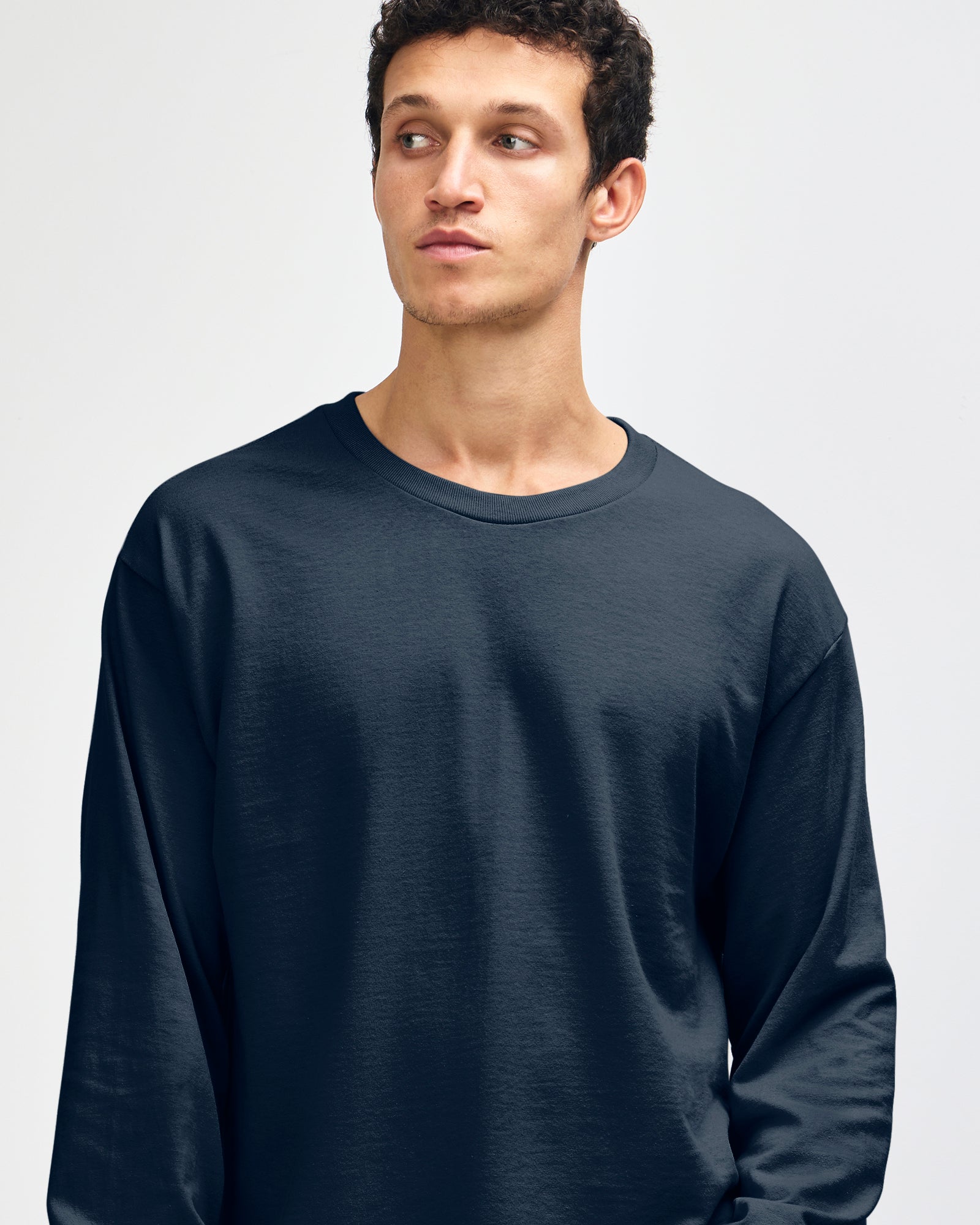 front view of a male Model wearing a True Navy colored Heavyweight Unisex Long Sleeve Crew Neck Tee, paired with blue jeans, standing against a plain background (front pose) -true navy