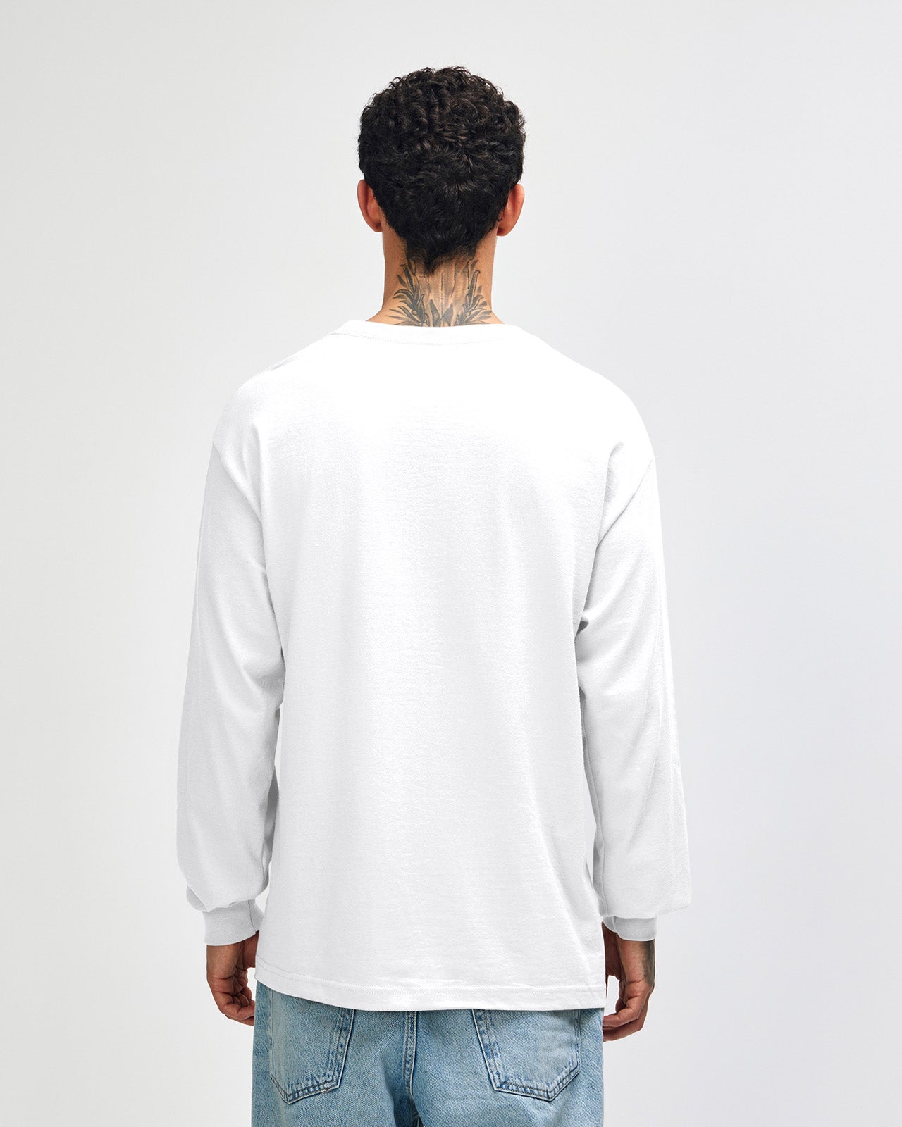 back view of a male Model wearing a White colored Heavyweight Unisex Long Sleeve Crew Neck Tee, paired with blue jeans, standing against a plain background (back pose) -white
