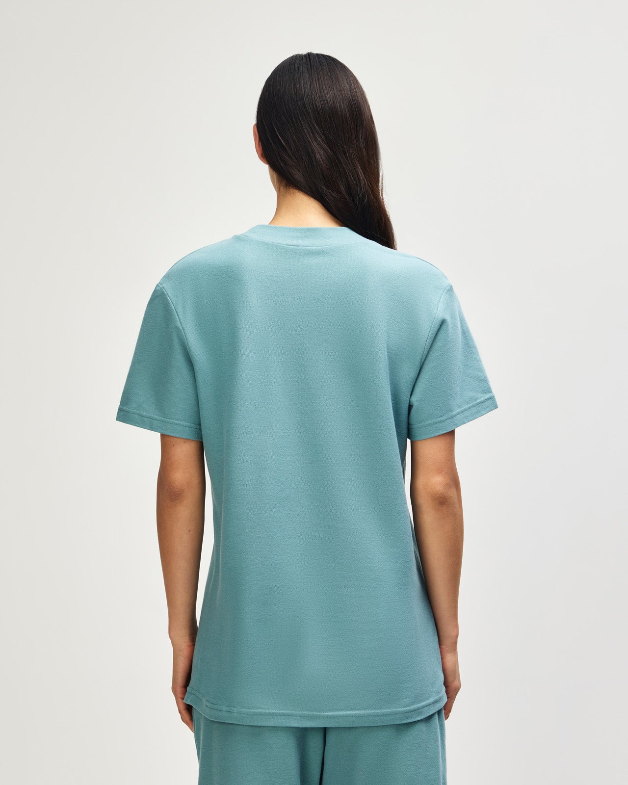 Female model wearing a Pique Unisex Mockneck Tee (back pose) -arctic