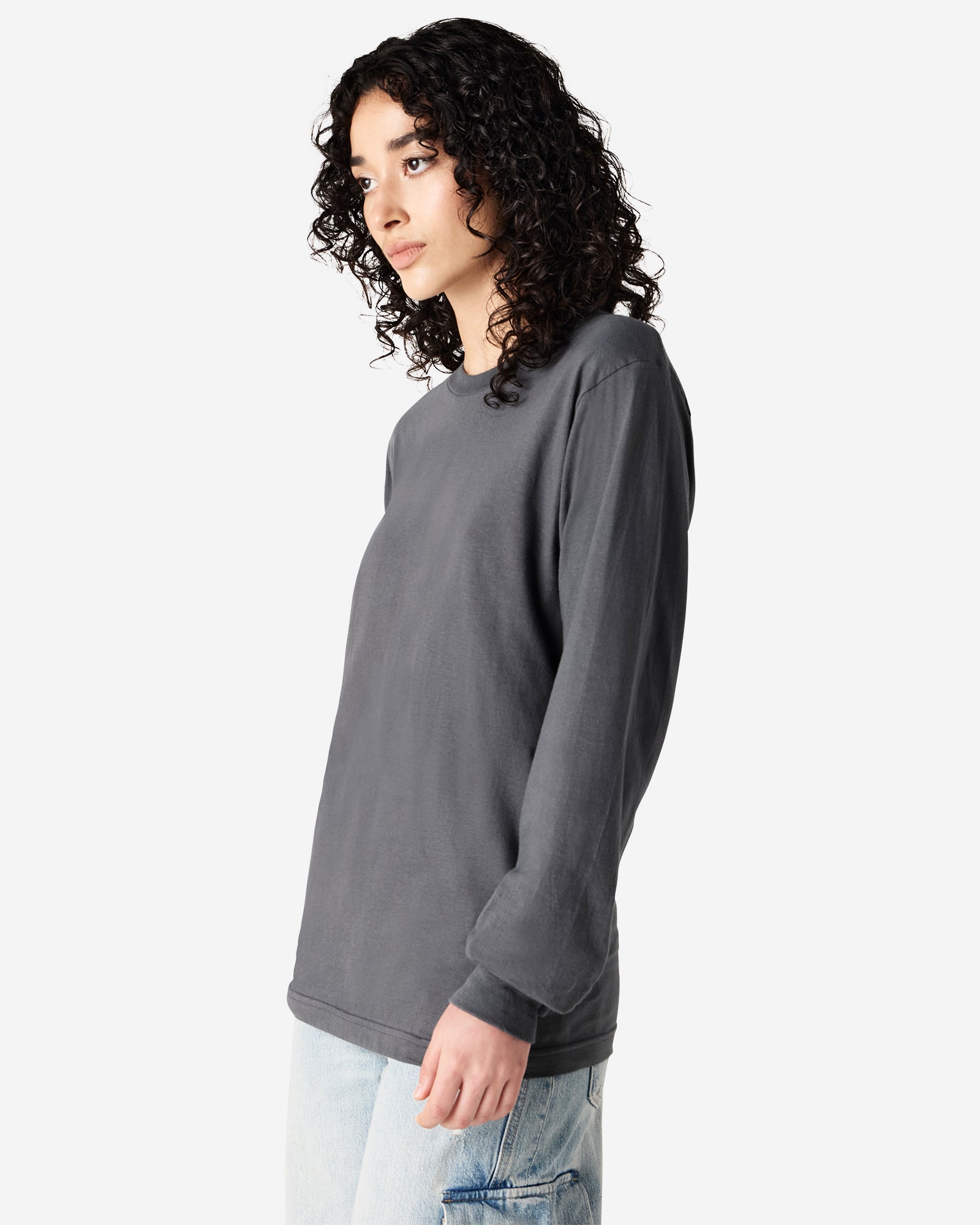 Female model wearing American Apparel Asphalt Colour Fine Jersey Unisex Long Sleeve Crew Neck Tee (Side pose) -asphalt