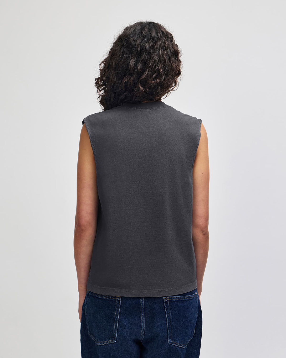 A person shown from the back wearing a dark charcoal gray sleeveless top and dark blue jeans against a light gray studio background. -Faded Black