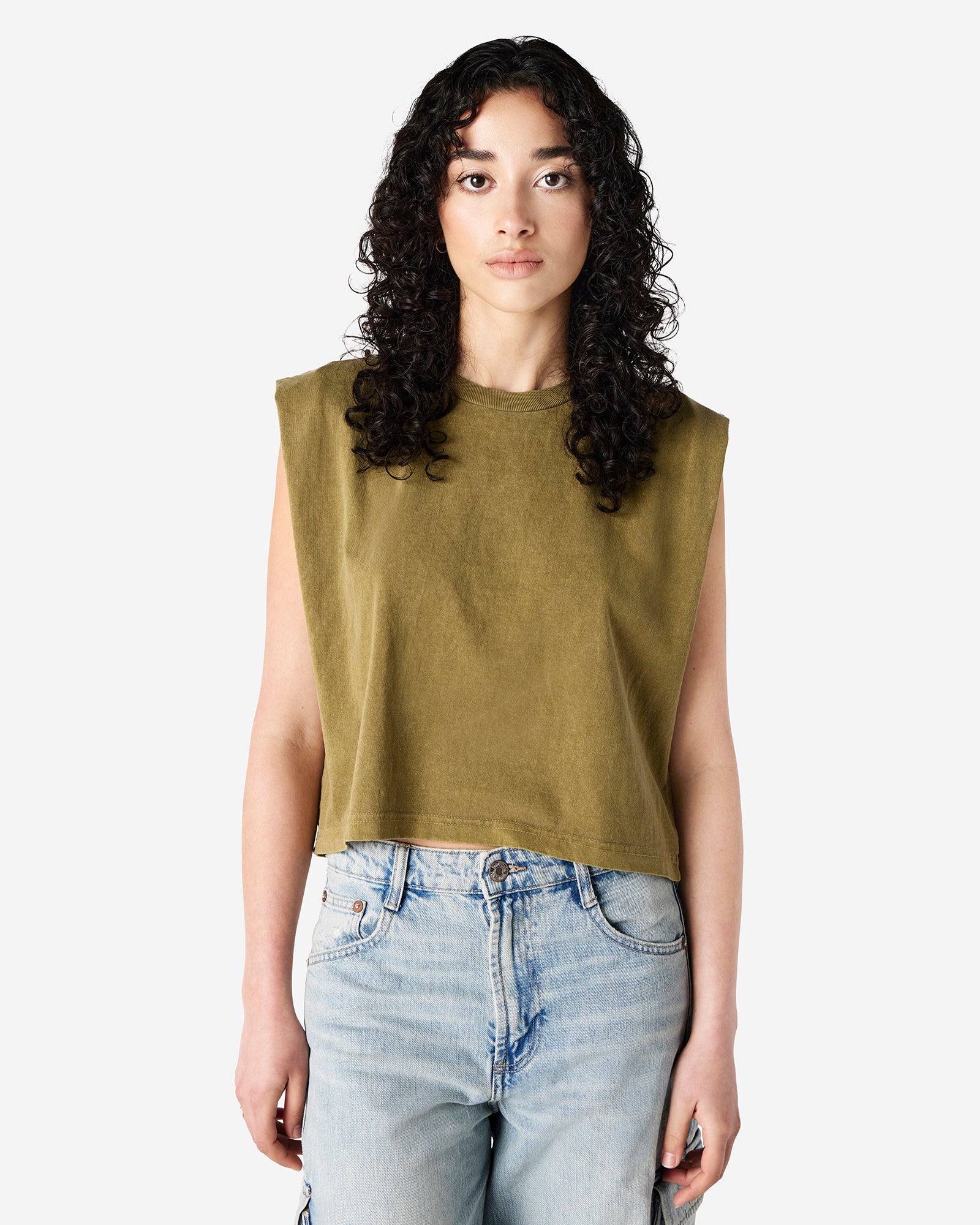 Model wearing a faded army Garment Dyed Women's Muscle Tee, sleeveless, paired with light blue jeans, standing against a plain white background (front pose) -army