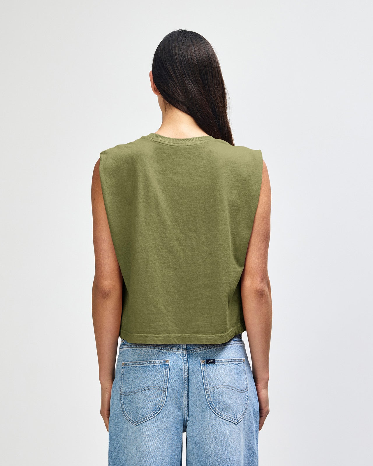 Model wearing a faded army Garment Dyed Women's Muscle Tee, sleeveless, paired with light blue jeans, standing against a plain white background (front pose) -army