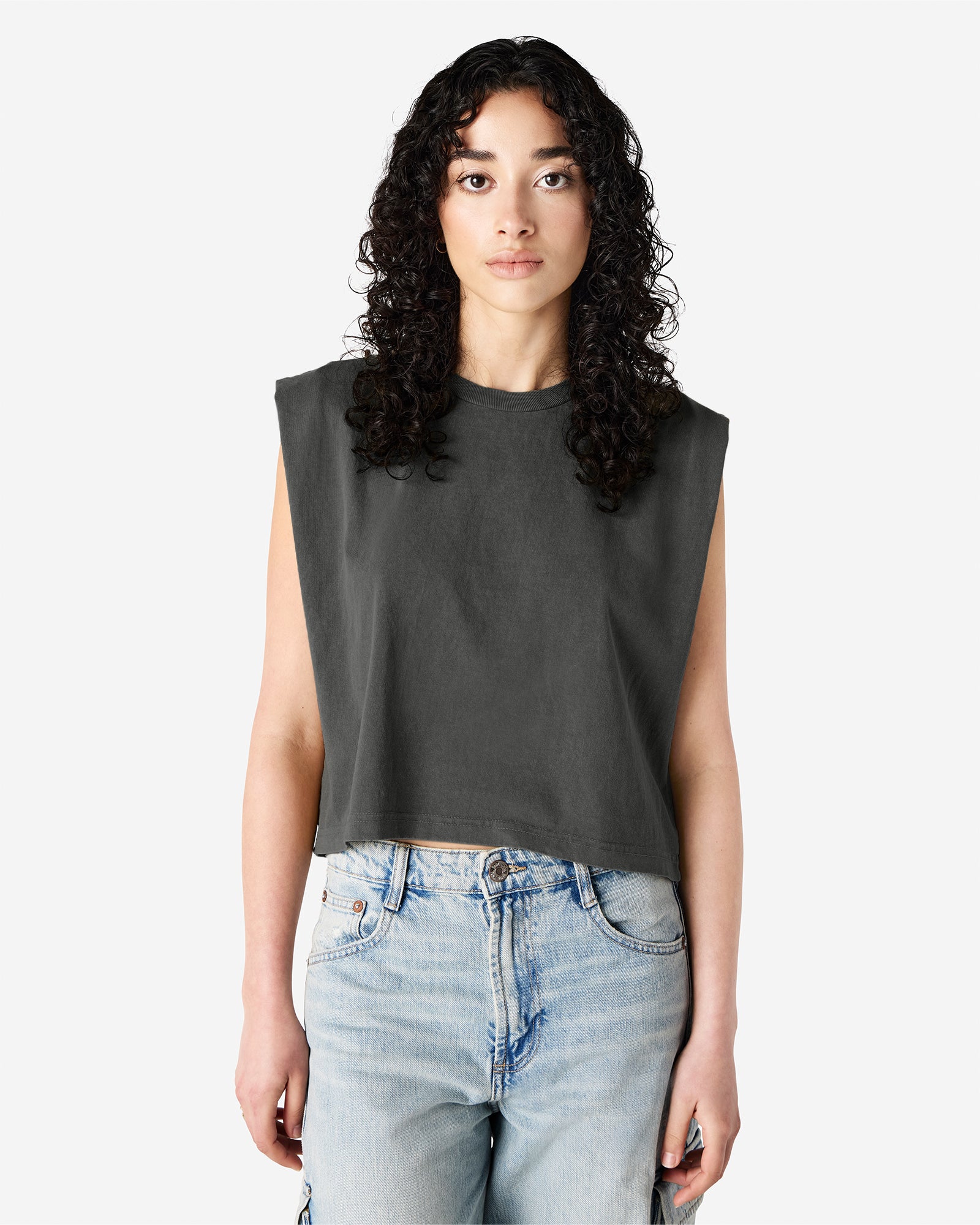 Model wearing a faded black Garment Dyed Women's Muscle Tee, sleeveless, paired with light blue jeans, standing against a plain white background (front pose) -black