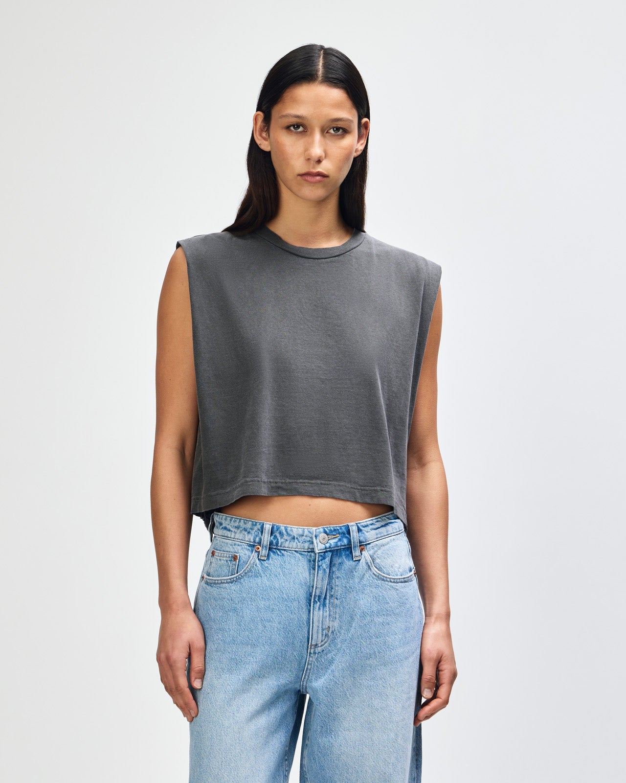 Model wearing a faded black Garment Dyed Women's Muscle Tee, sleeveless, paired with light blue jeans, standing against a plain white background (front pose) -black