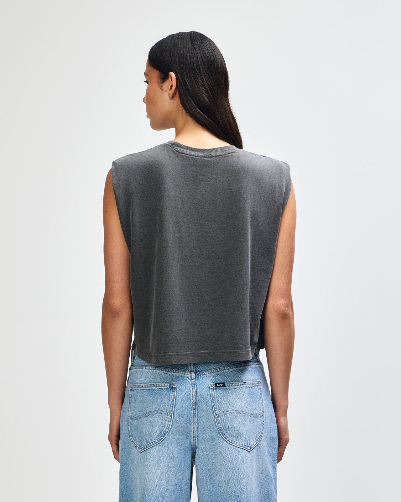 Model wearing a faded black Garment Dyed Women's Muscle Tee, sleeveless, paired with light blue jeans, standing against a plain white background (front pose) -black