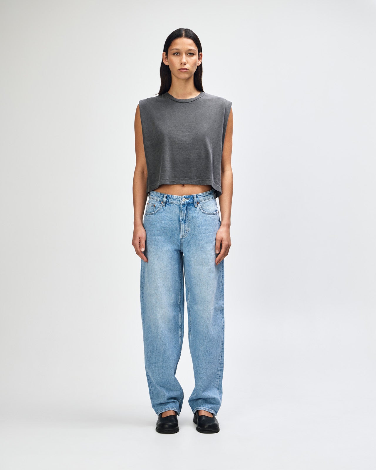 Model wearing a faded black Garment Dyed Women's Muscle Tee, sleeveless, paired with light blue jeans, standing against a plain white background (front pose) -black