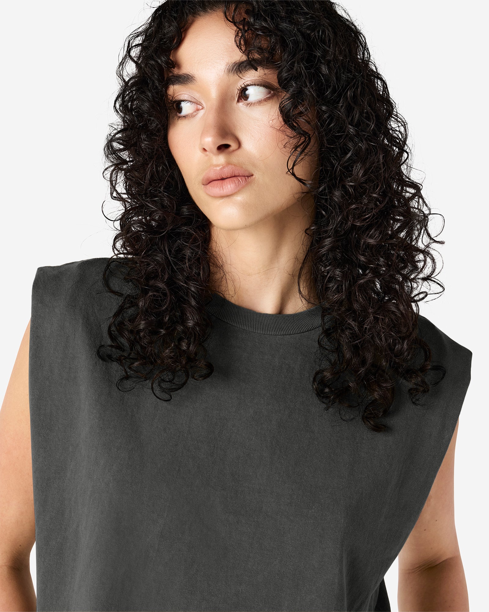 Model wearing a faded black Garment Dyed Women's Muscle Tee, sleeveless, paired with light blue jeans, standing against a plain white background (front pose) -black