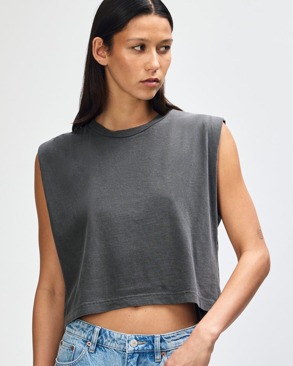 image of Women's Muscle T-Shirt : Model wearing a faded black Garment Dyed Women's Muscle Tee, sleeveless, paired with light blue jeans, standing against a plain white background (front pose) -black