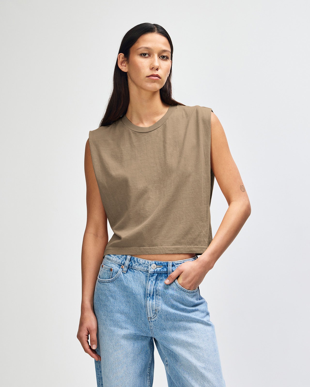 Model wearing a faded brown Garment Dyed Women's Muscle Tee, sleeveless, paired with light blue jeans, standing against a plain white background (front pose) -brown