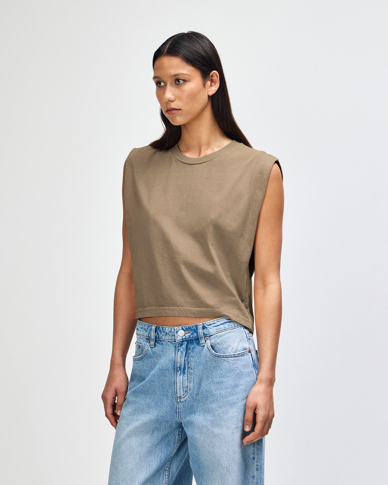 Model wearing a faded brown Garment Dyed Women's Muscle Tee, sleeveless, paired with light blue jeans, standing against a plain white background (front pose) -brown