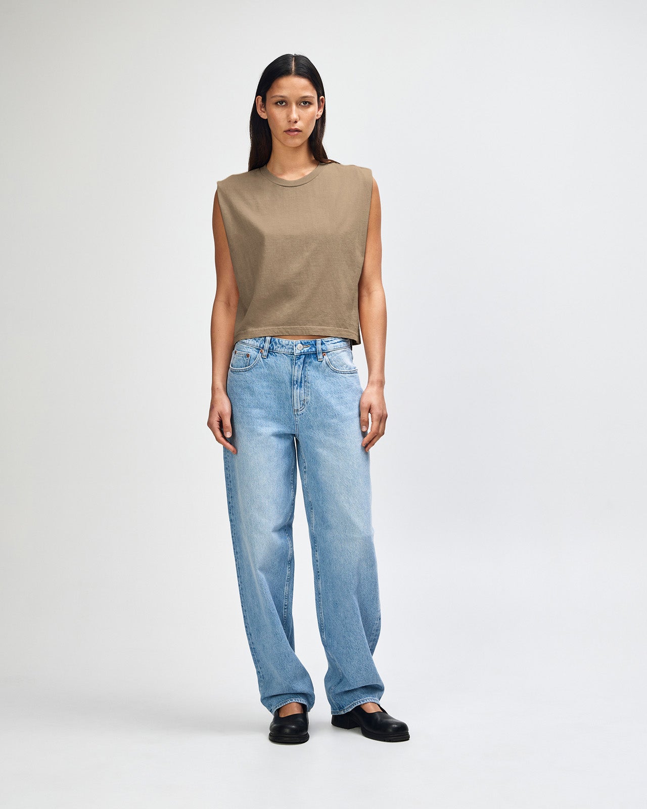 Model wearing a faded brown Garment Dyed Women's Muscle Tee, sleeveless, paired with light blue jeans, standing against a plain white background (front pose) -brown