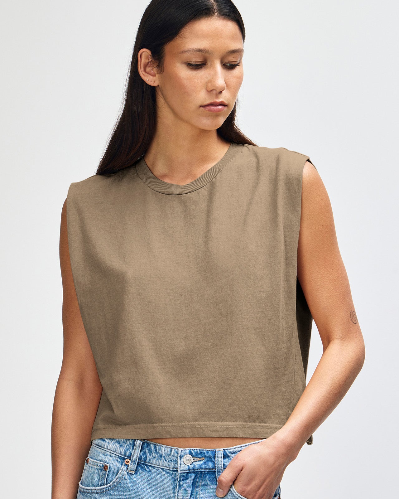 Model wearing a faded brown Garment Dyed Women's Muscle Tee, sleeveless, paired with light blue jeans, standing against a plain white background (front pose) -brown