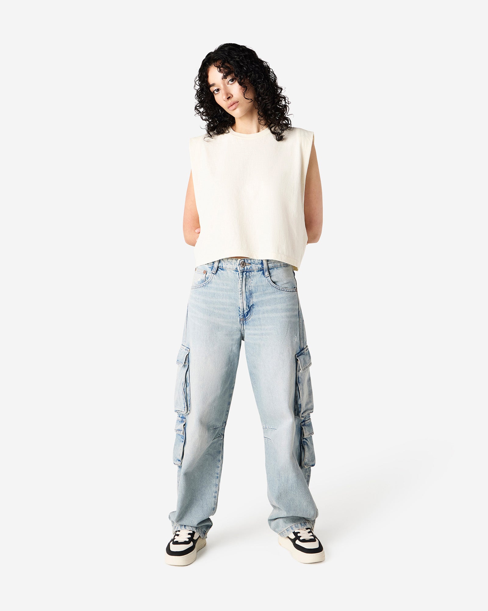 Model wearing a faded cream Garment Dyed Women's Muscle Tee, sleeveless, paired with light blue jeans, standing against a plain white background (front pose) -cream