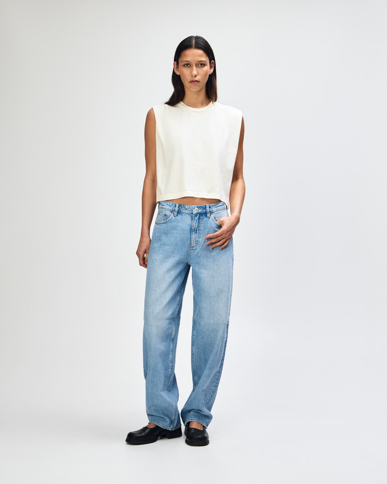 Model wearing a faded cream Garment Dyed Women's Muscle Tee, sleeveless, paired with light blue jeans, standing against a plain white background (front pose) -cream