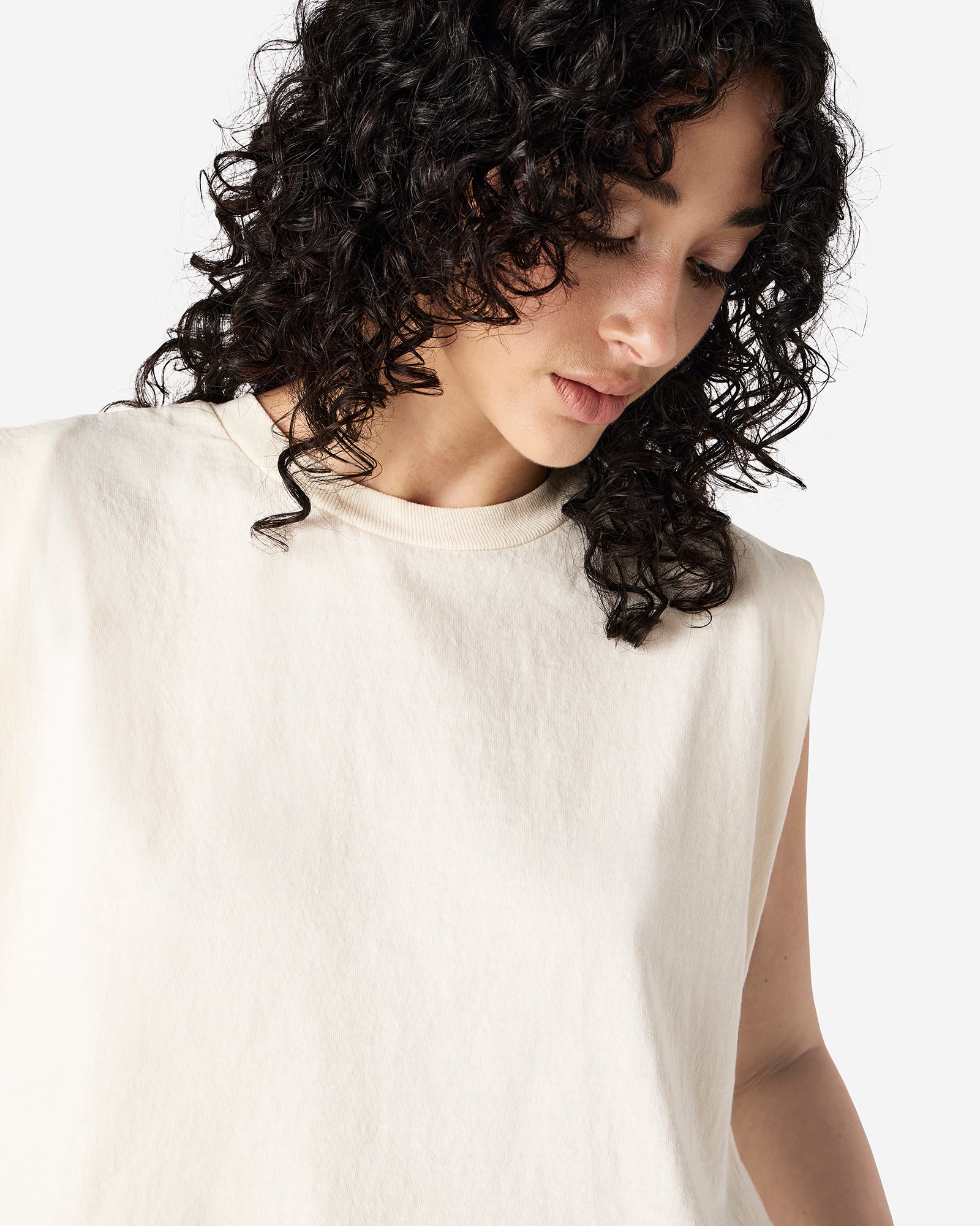 Model wearing a faded cream Garment Dyed Women's Muscle Tee, sleeveless, paired with light blue jeans, standing against a plain white background (front pose) -cream