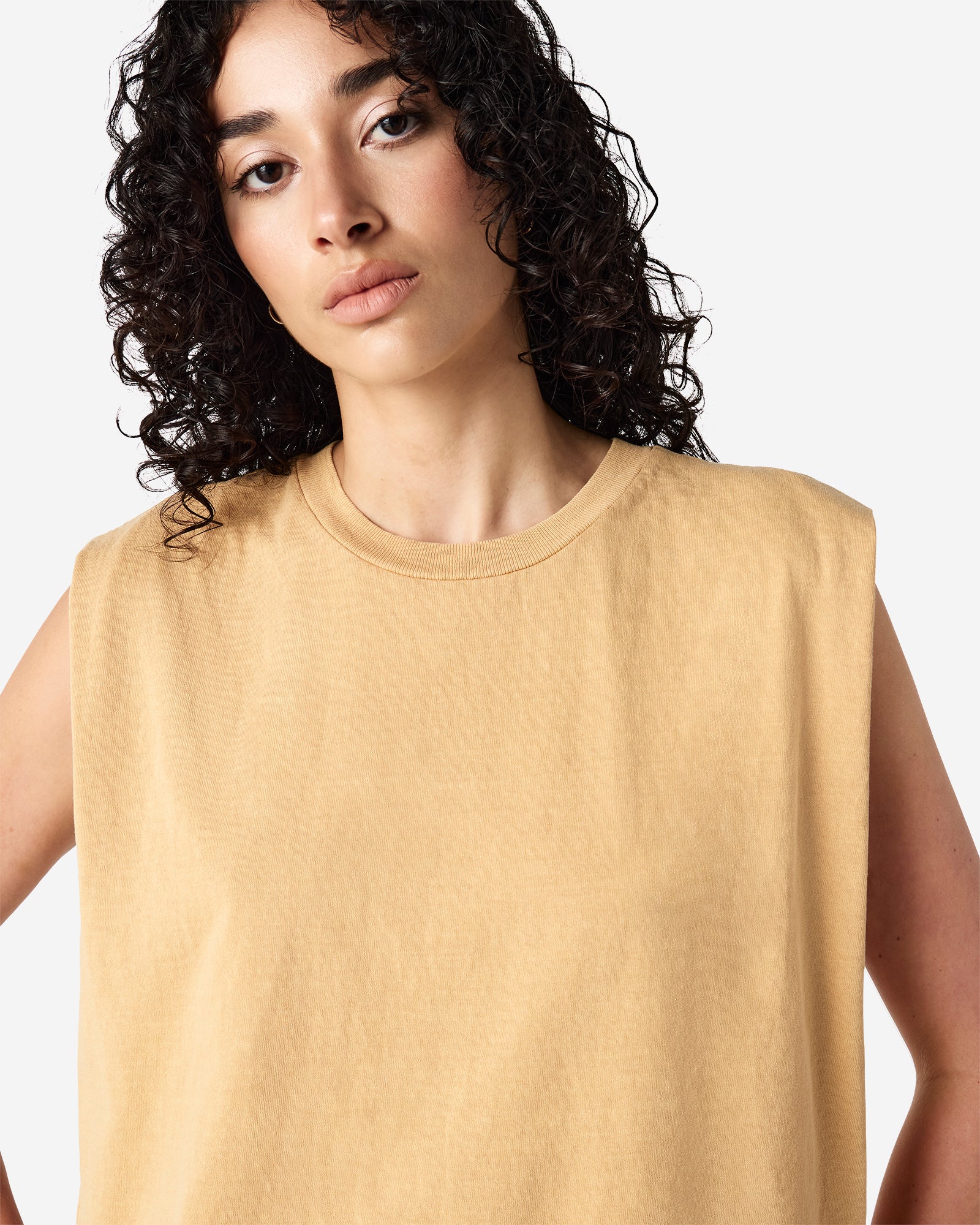 Model wearing a faded mustard Garment Dyed Women's Muscle Tee, sleeveless, paired with light blue jeans, standing against a plain white background (front pose) -mustard