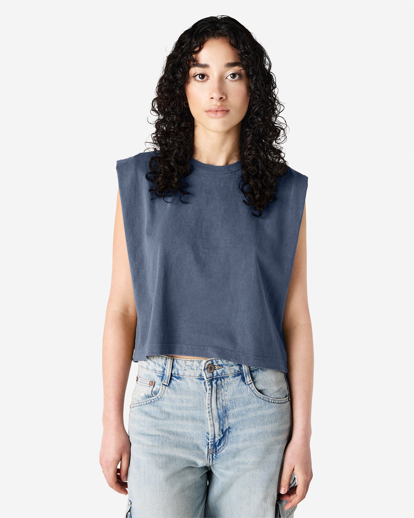 Model wearing a faded navy Garment Dyed Women's Muscle Tee, sleeveless, paired with light blue jeans, standing against a plain white background (front pose) -navy