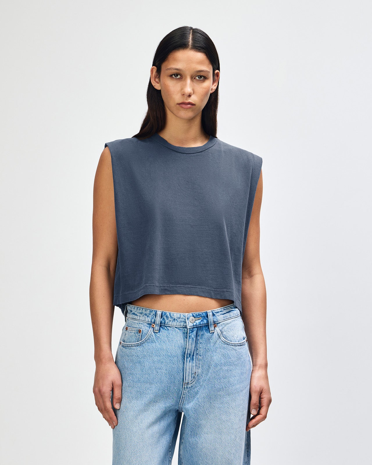 Model wearing a faded navy Garment Dyed Women's Muscle Tee, sleeveless, paired with light blue jeans, standing against a plain white background (front pose) -navy