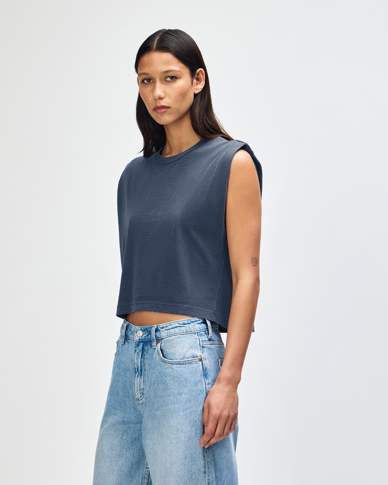 Model wearing a faded navy Garment Dyed Women's Muscle Tee, sleeveless, paired with light blue jeans, standing against a plain white background (front pose) -navy