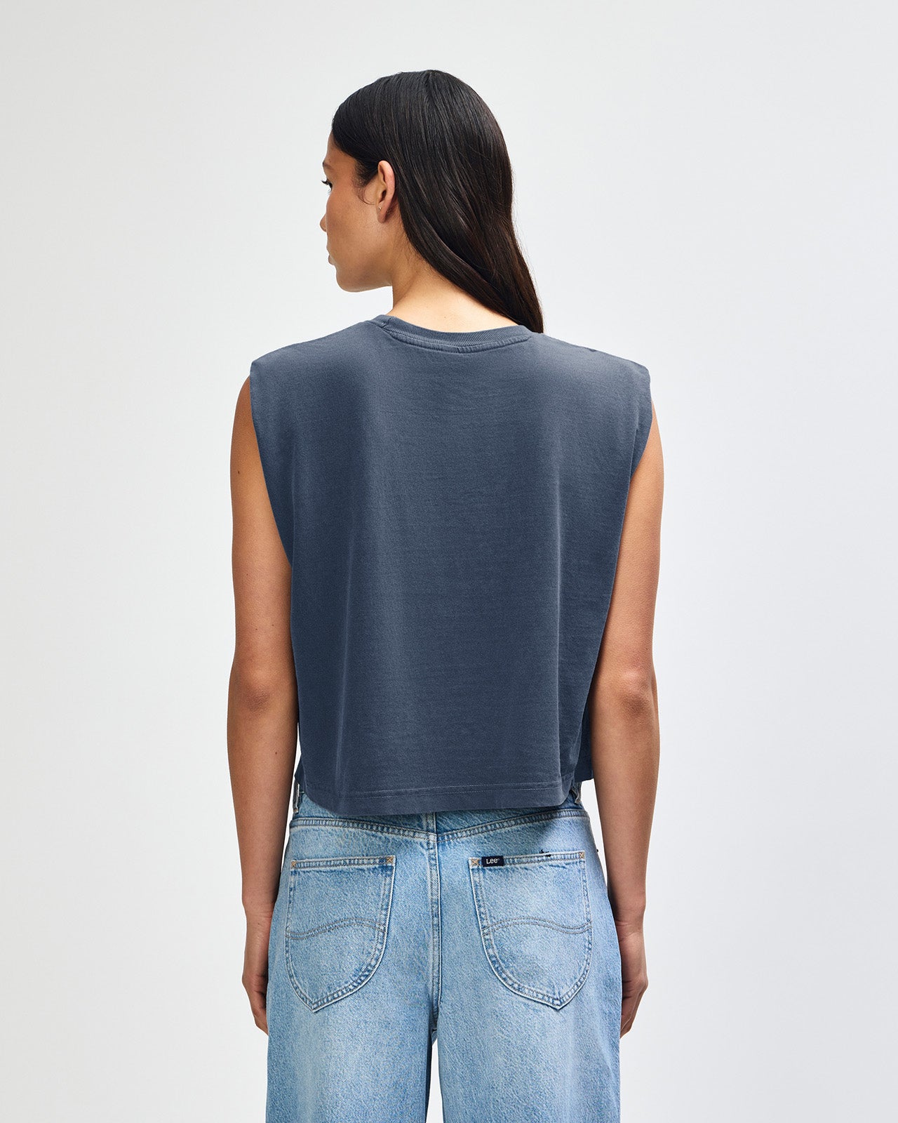 Model wearing a faded navy Garment Dyed Women's Muscle Tee, sleeveless, paired with light blue jeans, standing against a plain white background (front pose) -navy
