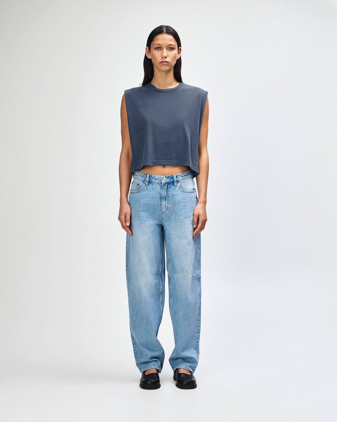 Model wearing a faded navy Garment Dyed Women's Muscle Tee, sleeveless, paired with light blue jeans, standing against a plain white background (front pose) -navy