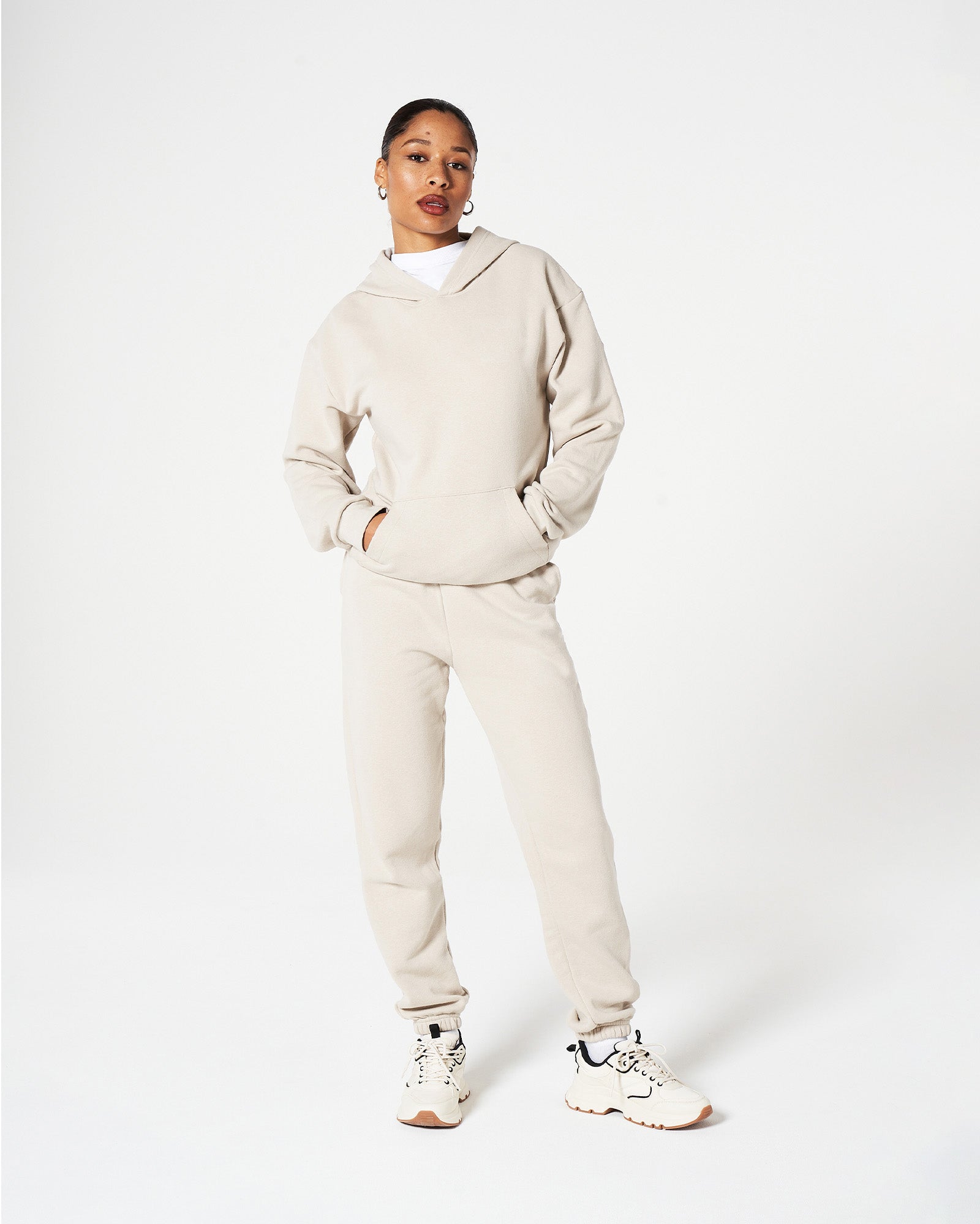 Female model wearing an American Apparel bone hoodie and sweatpants tracksuit set with hands in the pocket